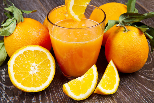 glass of fresh orange juice and oranges on wooden background