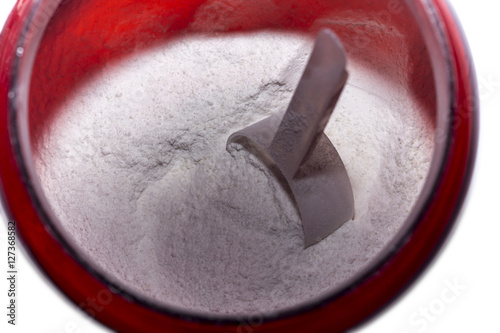 Pre-workout amino acids powder with scoop in red jar close up shot. 