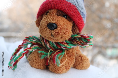 игрушечная собачка в шапке и шарфе сидит на снегу