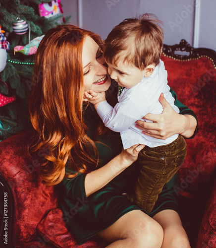 Happy mother and her cute little son sits in red armchair