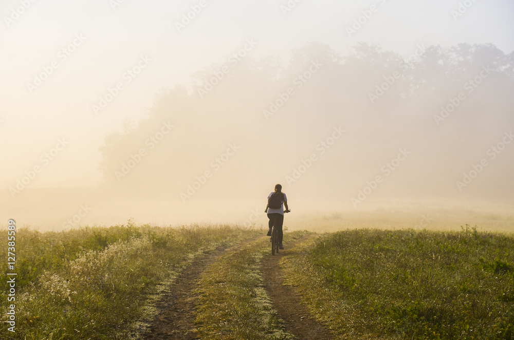 Girl ride on bicycle in autumn misty morning. Original sport wallaper