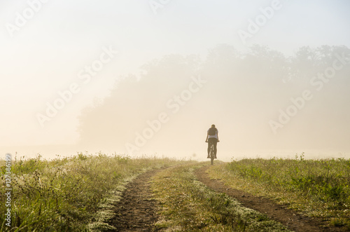 Small silhouette of man on bicycle in misty november active morning © kovop58