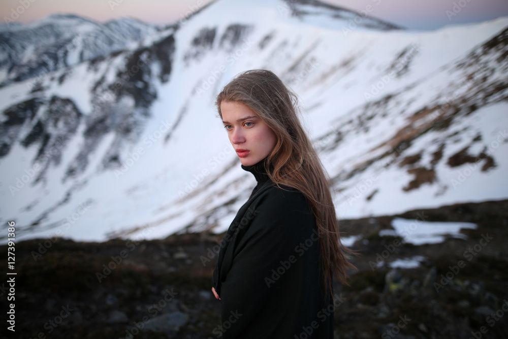 Young woman in long mystical dress looking into the sun stands on the top of the mountain. Woman on the background of snow winter and mounts. Travel inspiration and motivation, beautiful landscape. Young woman in long mystical dress looking into the sun stands on the top of the mountain. Woman on the background of snow winter and mounts. Travel inspiration and motivation, beautiful landscape.