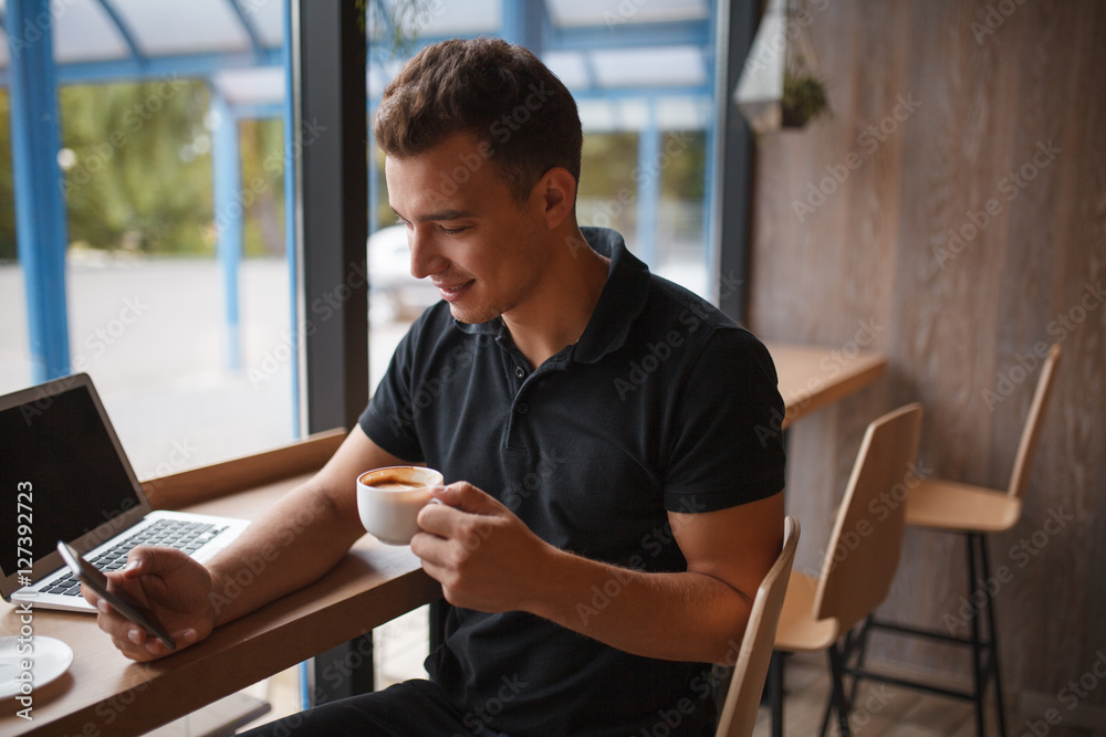 Young man using mobile phone and drinking coffee in cafe Young man using mobile phone and drinking coffee in cafe