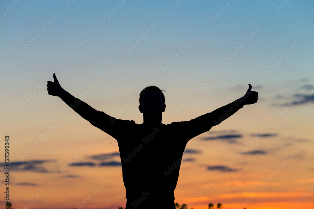 Silhouette of male celebrating with arm up towards the sunrise.