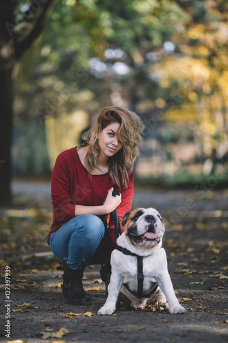 People and dogs outdoors. Beautiful and happy woman enjoying in autumn park walking with her adorable English bulldog. © Dusko