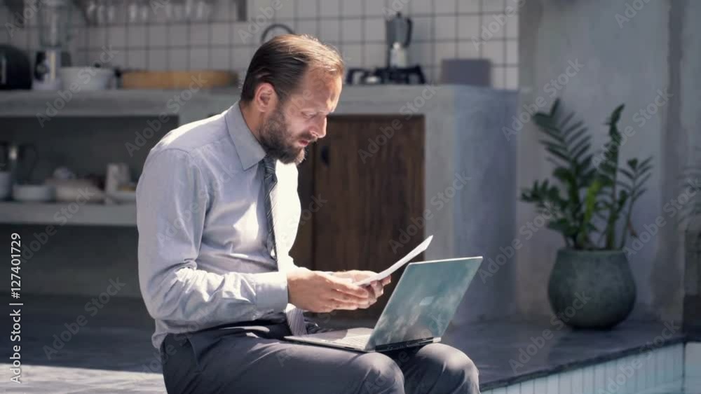 Overwhelmed businessman with documents and laptop sitting by pool in outdoor villa
Overwhelmed businessman with documents and laptop sitting by pool in outdoor villa