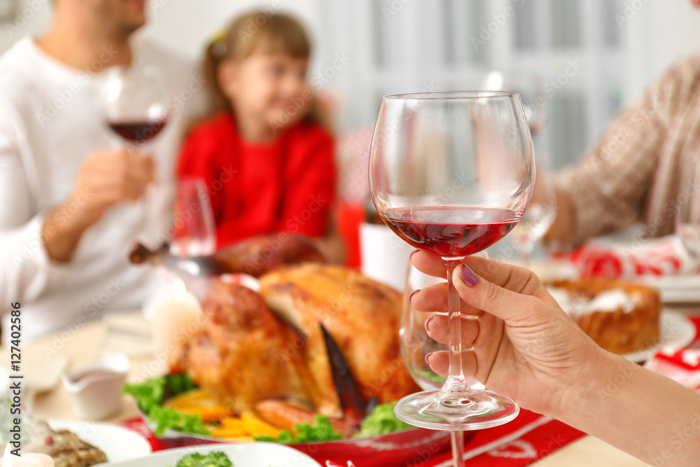 Female hand holding glass with red wine on blurred background, close up view