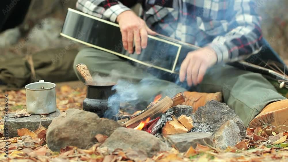 Man tourist with guitar makes coffee on campfire. Travel life. Vintage shoot.
Man tourist with guitar makes coffee on campfire. Travel life. Vintage shoot.