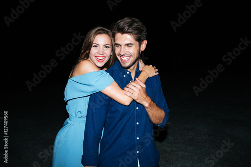 Cheerful young couple hugging on the beach at night