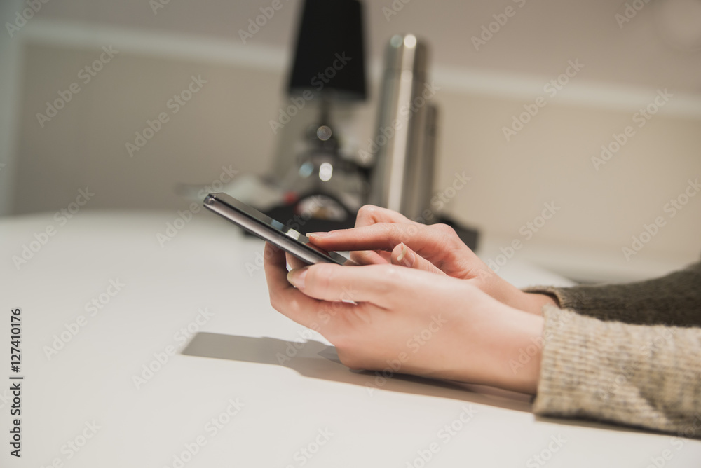 Close-up hands of the girl, sitting at the wooden table, holding smart phone