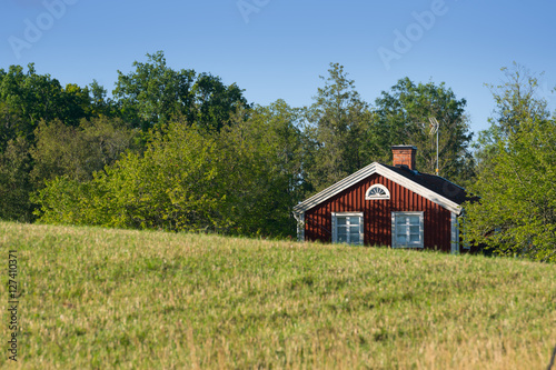 Old traditional red painted farmhouse in Sweden hidden behind hills. In the foreground landscape with meadows