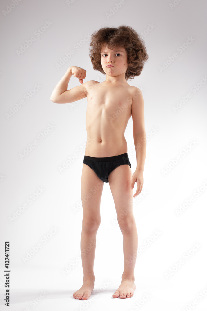 Curly boy in shorts showing a strong hand. He looks into the camera. White background. Curly boy in shorts showing a strong hand. He looks into the camera. White background.