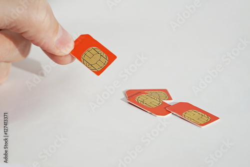 Isolated photo of male hand holding red SIM card above a group of 3 other SIM cards used in the mobile phones (cell phone devices) with a focus on their golden micro chip 