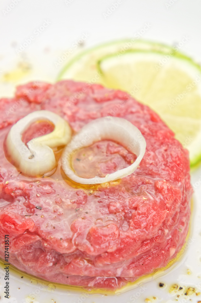 Steak tartare closeup with lemon slices on white plate Steak tartare closeup with lemon slices on white plate