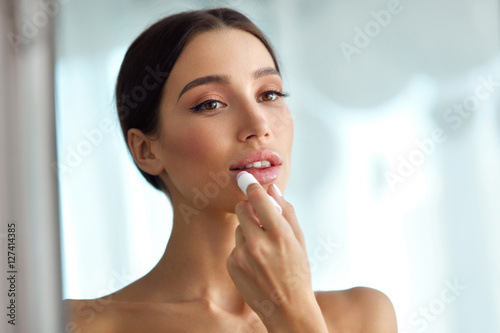 Fotografie Beautiful Woman With Beauty Face Applies Balm On Lips. Skin Care
