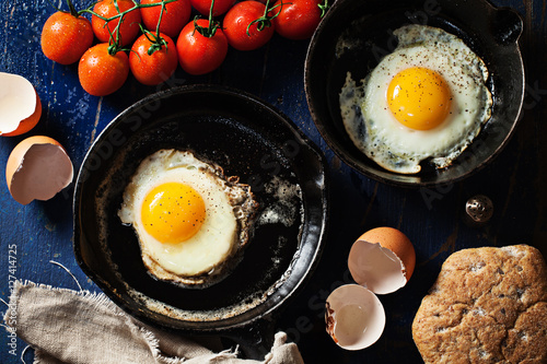 Fried eggs in skillets on wooden background