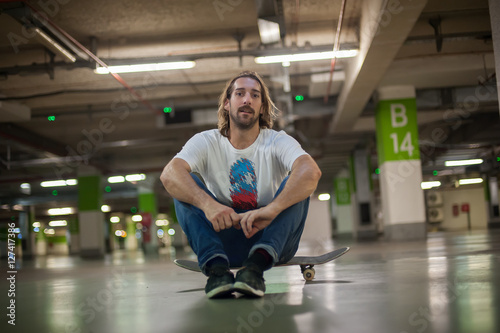 Skateboarder sitting on his skateboard in the underground garage