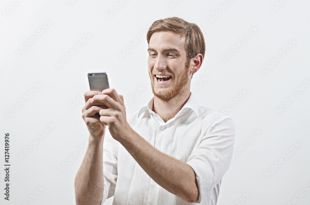 Very Happy Smiling Young Adult Man in White Shirt Looking at His Mobile Phone Very Happy Smiling Young Adult Man in White Shirt Looking at His Mobile Phone