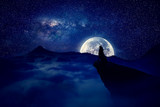 Lonely wolf silhouette howls on a cliff over full moon night background. Mysterious scene werewolf halloween scary view.