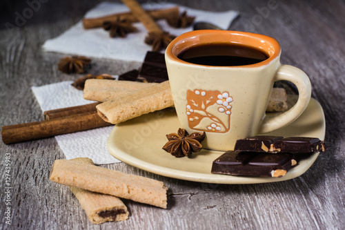 Чашка кофе, шоколад, печенье, бадьян и корица на деревянном столе