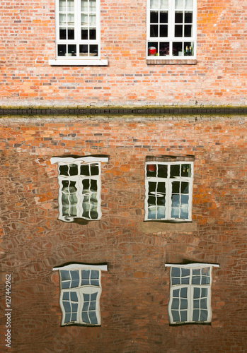 Abstract water reflections of old red brick buildings with windows in canal on a sunny day in England UK