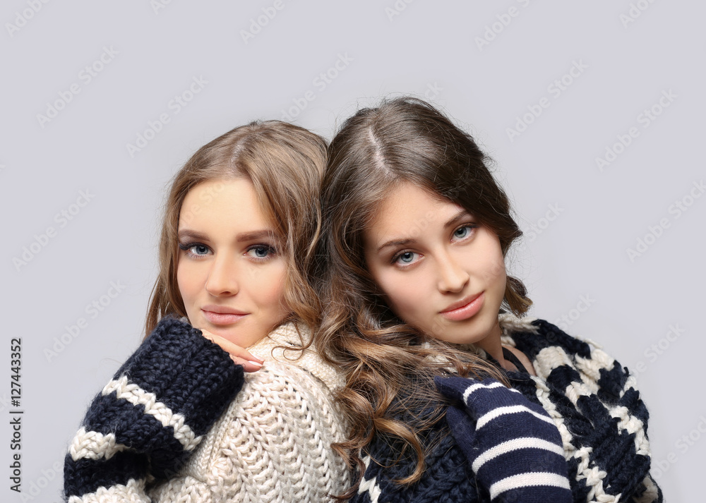 Two girl wearing knit hat, scarf, sweater and gloves posing against blue background. Two girl wearing knit hat, scarf, sweater and gloves posing against blue background.