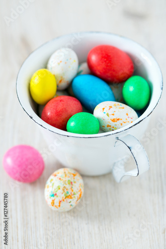 Easter candy eggs in miniature cup on wooden surface