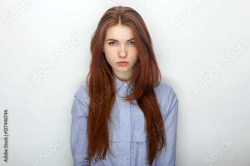 Young serious angry redhead beautiful woman in shirt portrait on a white background