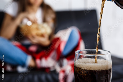 Girl eating chips, sitting on sofa. Fosuc  glass of soda. photo