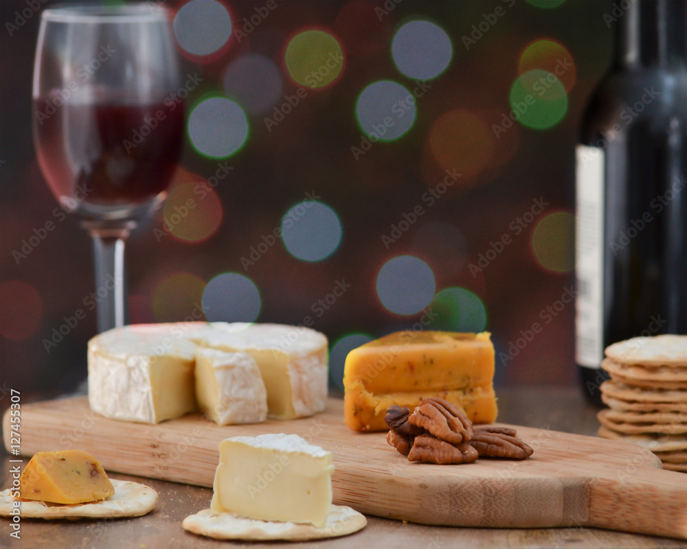 Brie, pepper jack, pecan halves and crackers on wooden cheese board, with one bottle and one glass of red wine, against dark holiday lights background - celebrating alone concept Brie, pepper jack, pecan halves and crackers on wooden cheese board, with one bottle and one glass of red wine, against dark holiday lights background - celebrating alone concept