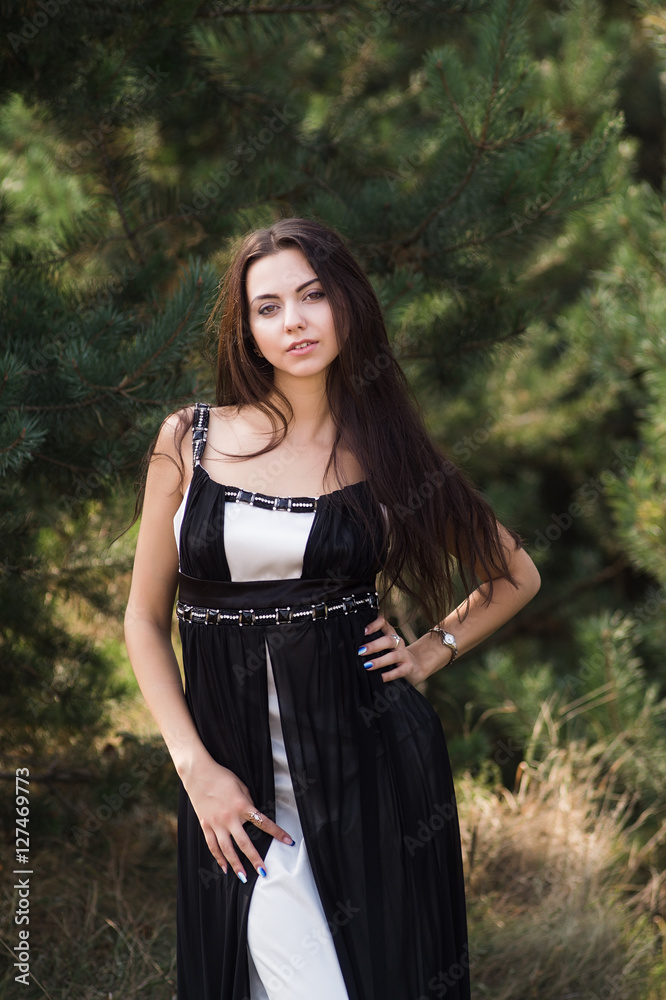 Graceful charming brunette model posing in black dress in coniferous park