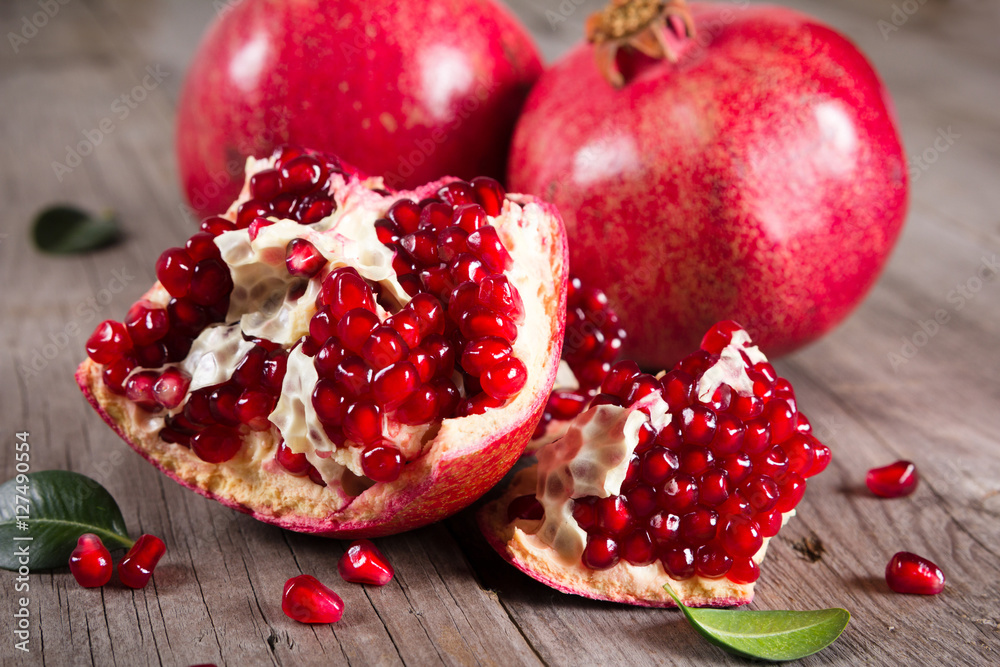 Whole and broken red ripe juicy pomegranates on rustic wooden unpainted table Whole and broken red ripe juicy pomegranates on rustic wooden unpainted table