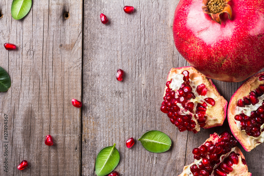 Broken and whole red ripe juicy pomegranates on rustic wooden unpainted table Broken and whole red ripe juicy pomegranates on rustic wooden unpainted table