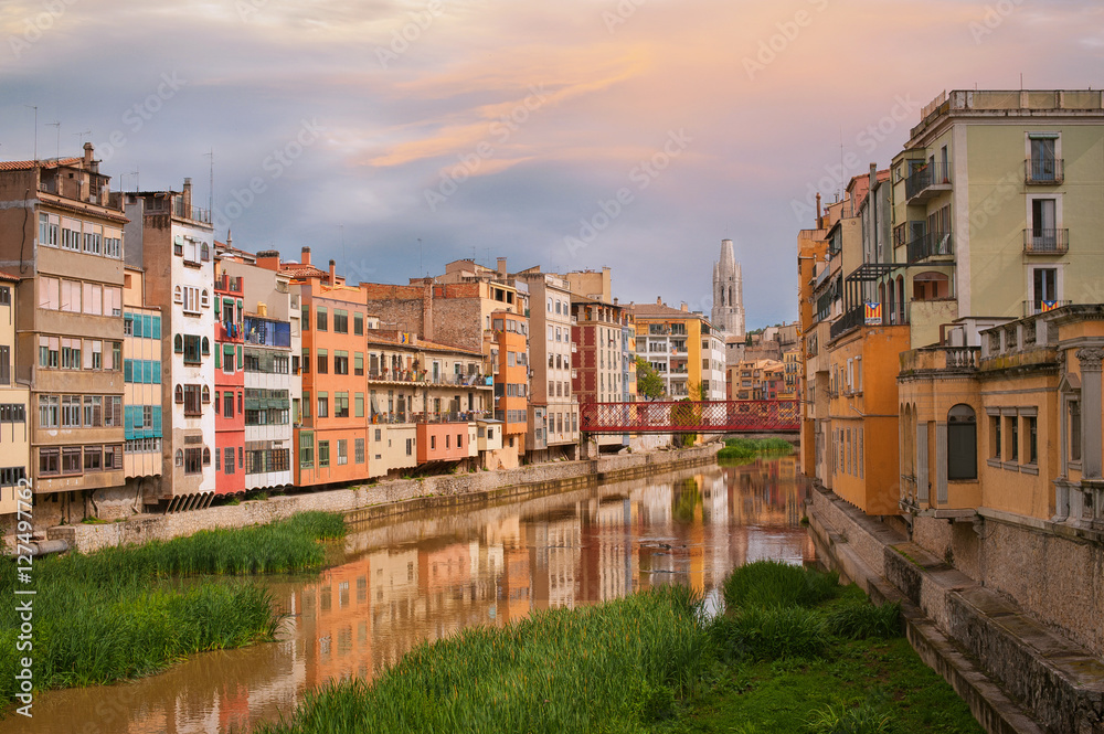 Colorful yellow and orange houses and bridge Pont de Sant Agusti reflected in water river Onyar, in Girona, Catalonia, Spain. Church of Sant Feliu and Saint Mary Cathedral at background.
