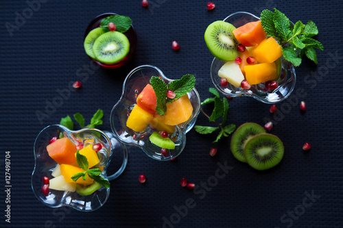 Fototapeta Naklejka Na Ścianę i Meble -  Fruit desserts, salad of pineapple, papaya, pomegranate and mint, kiwi on a dark background
