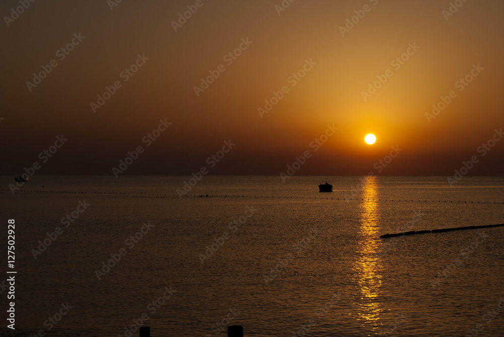 Sunrise with reflection on sea water scale of dark orange color and boat