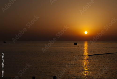 Obraz na płótnie Sunrise with reflection on sea water scale of dark orange color and boat w salonie