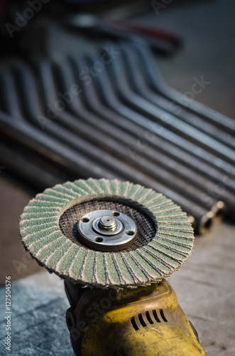 Angle grinder with rotary blade and metal pipe blurred in the background