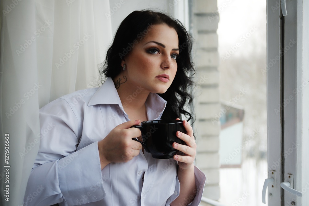 Beautiful girl looks out of window and holds a cup. Winter morning. Beautiful girl looks out of window and holds a cup. Winter morning.