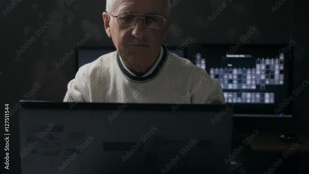 Senior man working at a laptop in dark room