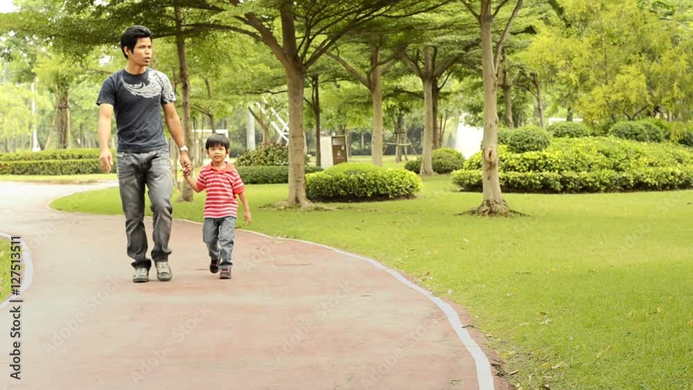 An Asian father points something out while walking in the park with his son. An Asian father points something out while walking in the park with his son.