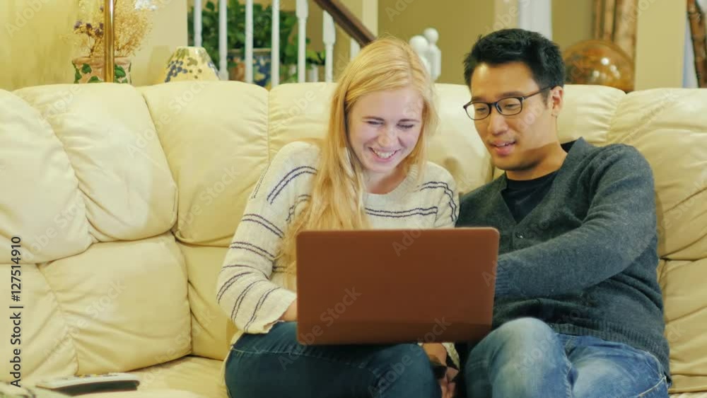 Friends - Korean man and Caucasian woman resting at home. Enjoy a laptop, a good time Friends - Korean man and Caucasian woman resting at home. Enjoy a laptop, a good time