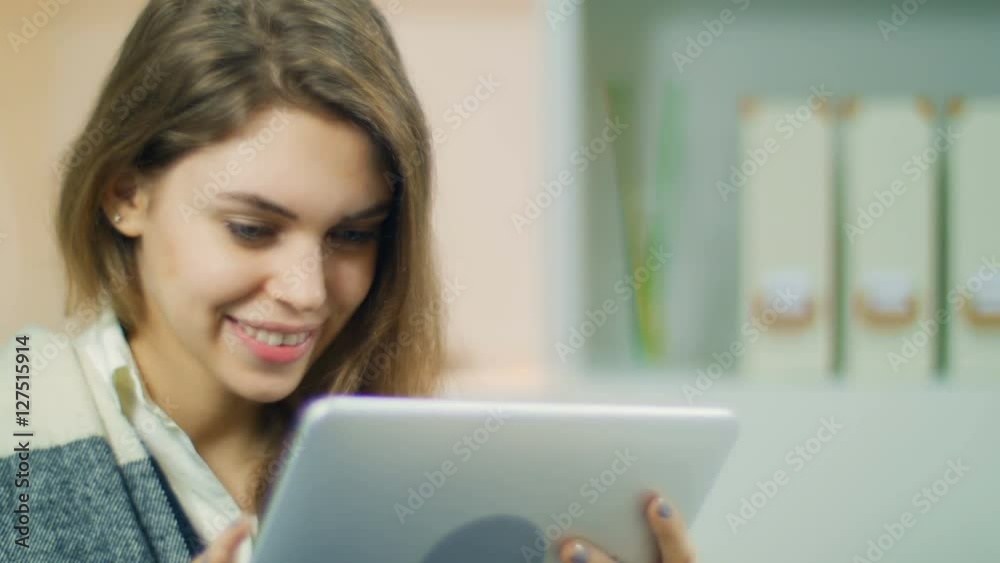 The young girl smiles broadly communicates with friends on the tablet The young girl smiles broadly communicates with friends on the tablet