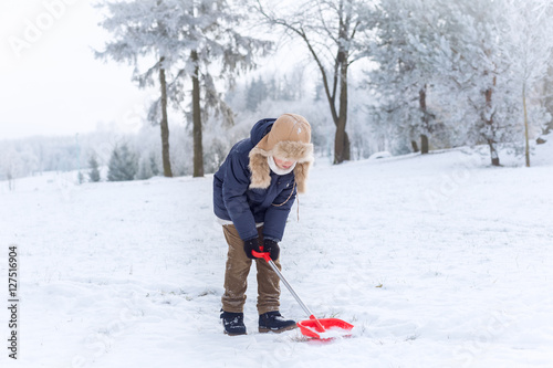Child with a red shovel on a snowy day in a park © taniasv