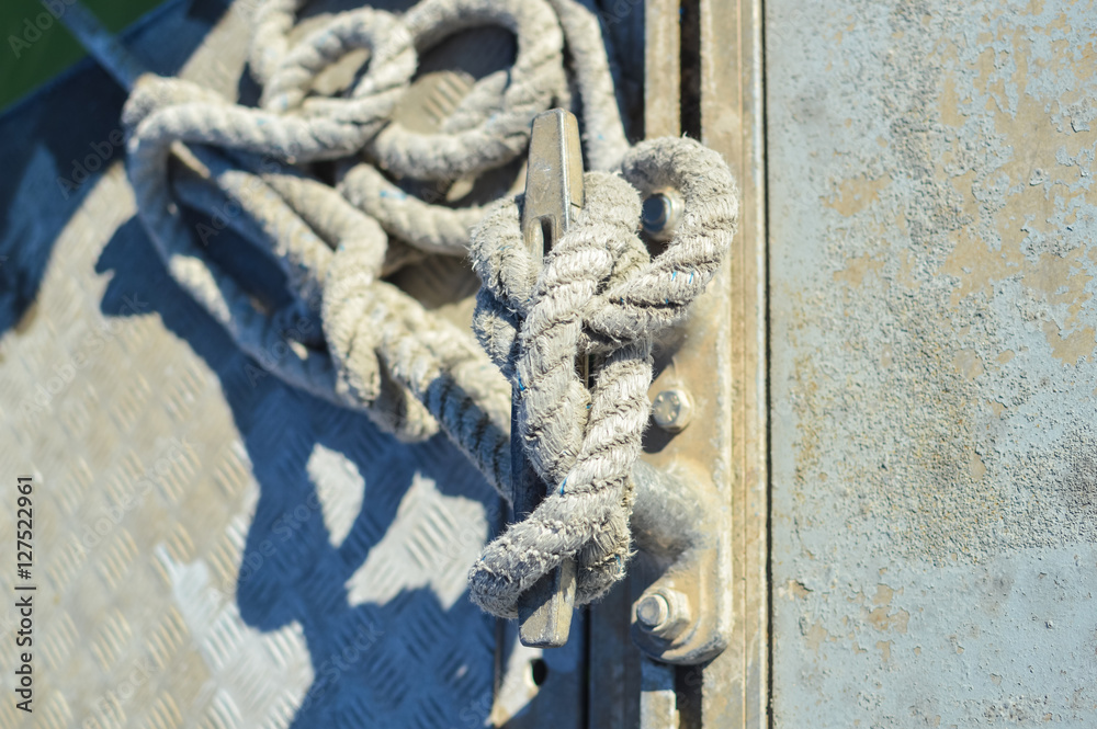 Fototapeta premium Closeup on mooring bollard with rope tied on pier by the sea outdoors background