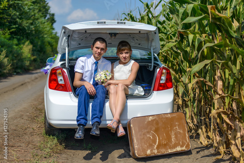 Young newlyweds sitting in open car trunk