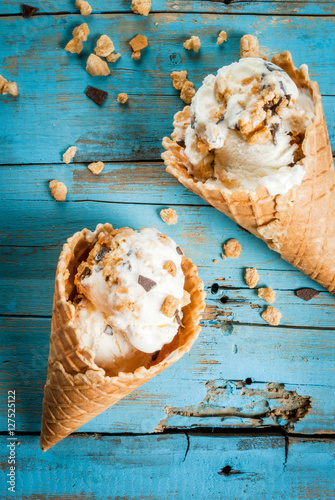 Two ice cream cones with sprinkles of chocolate and cookies on a bright blue wooden table. Summer, bright sun. Top view, copy space