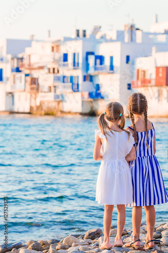 Little kids at Little Venice the most popular tourist area on Mykonos island, Greece. Back view of beautiful girls look at Little Venice background.