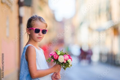Adorable little girl with flowers bouquet walking in european city
